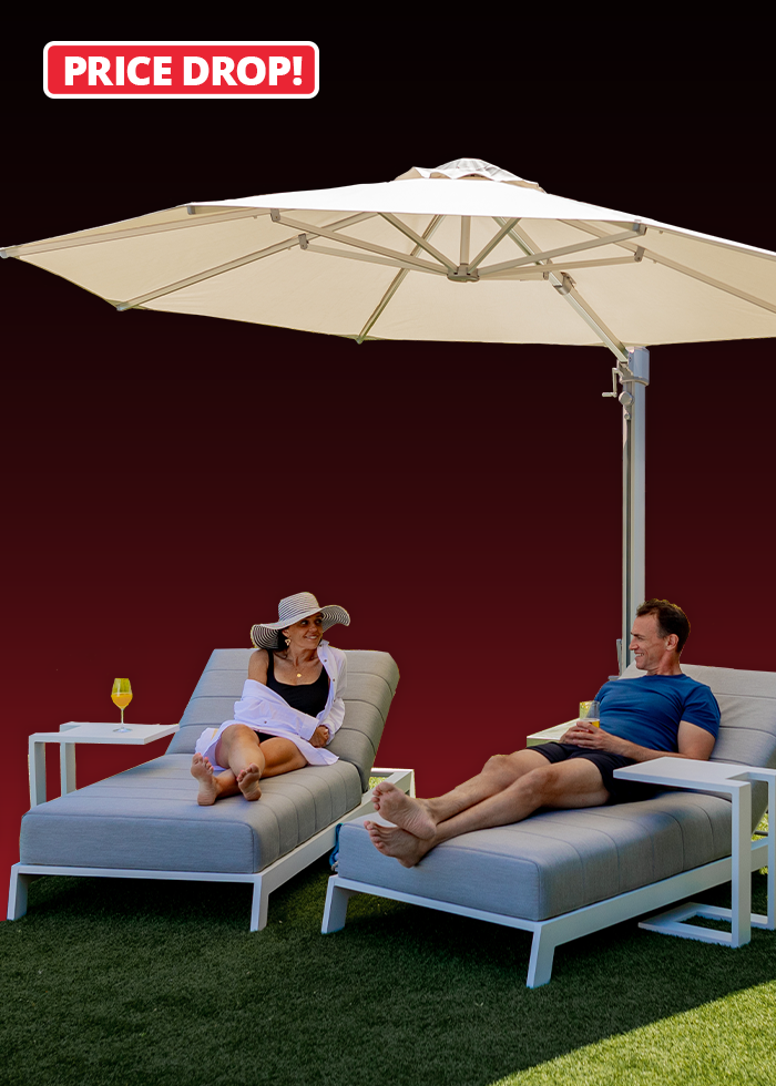 A woman and a man relax on outdoor loungers under a large white sun umbrella, with a "Price Drop!" label above.