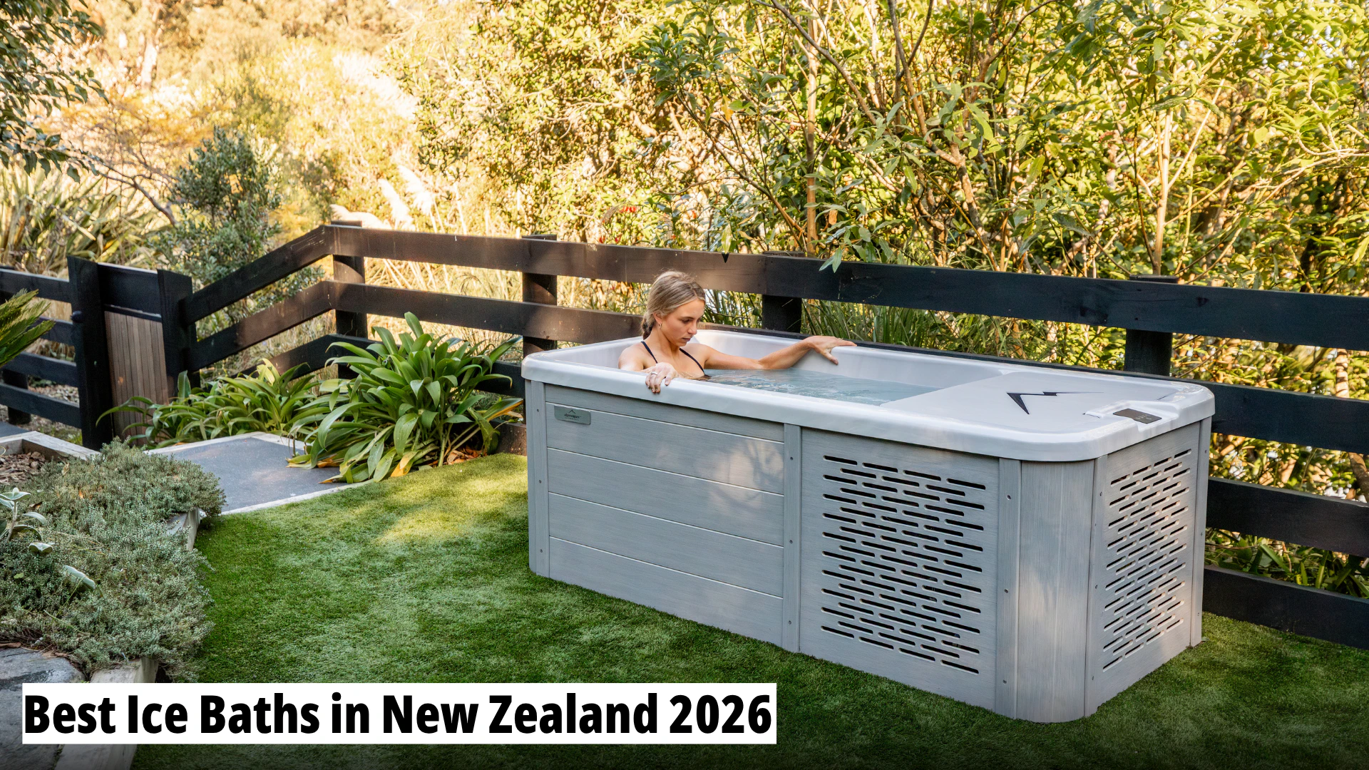 A woman relaxes in an outdoor ice bath on artificial grass next to a wooden fence and lush greenery, with the text "Best Ice Baths in New Zealand 2026" overlaid.