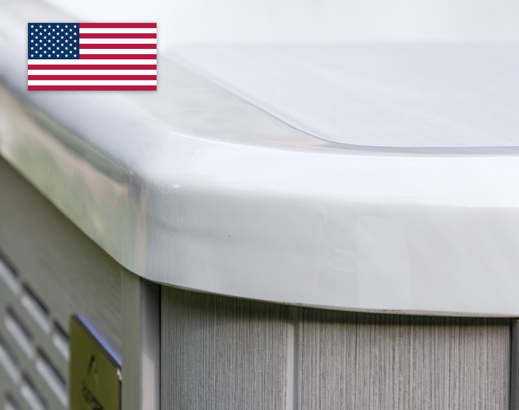 Close-up of a white acrylic shell corner on a light grey outdoor unit, with a small American flag in the top left corner.