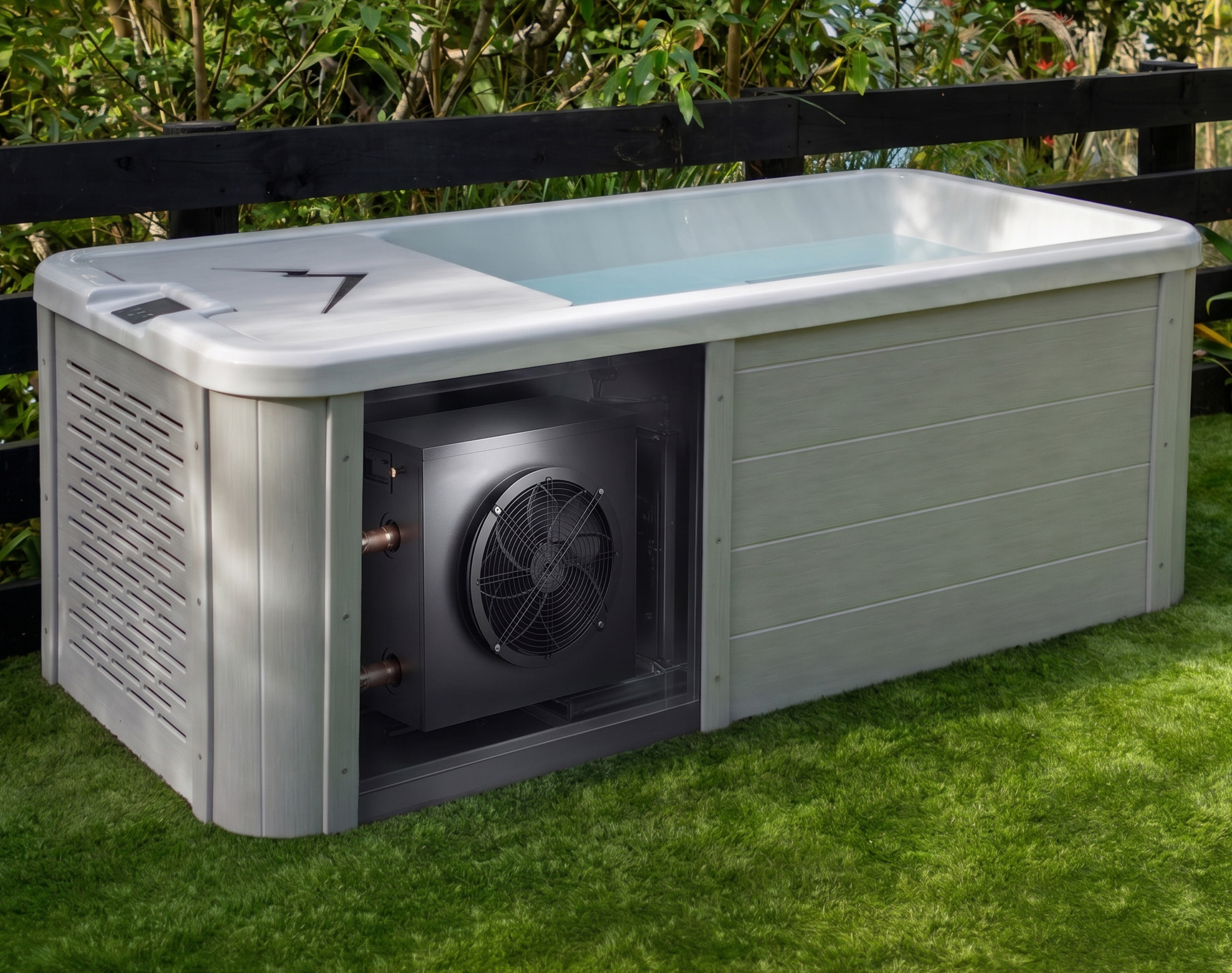 A rectangular outdoor bath with a visible built-in chiller system on one end, placed on grass near a wooden fence and greenery.