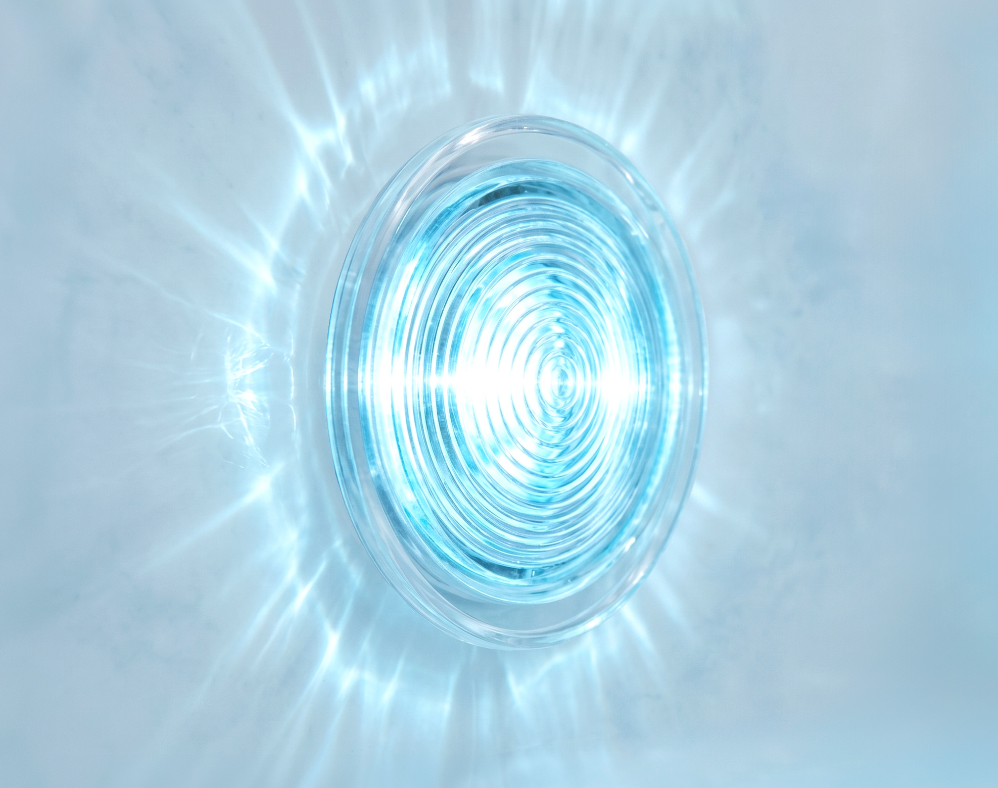 A round underwater light emits a bright blue glow, casting rippled reflections on a smooth surface.