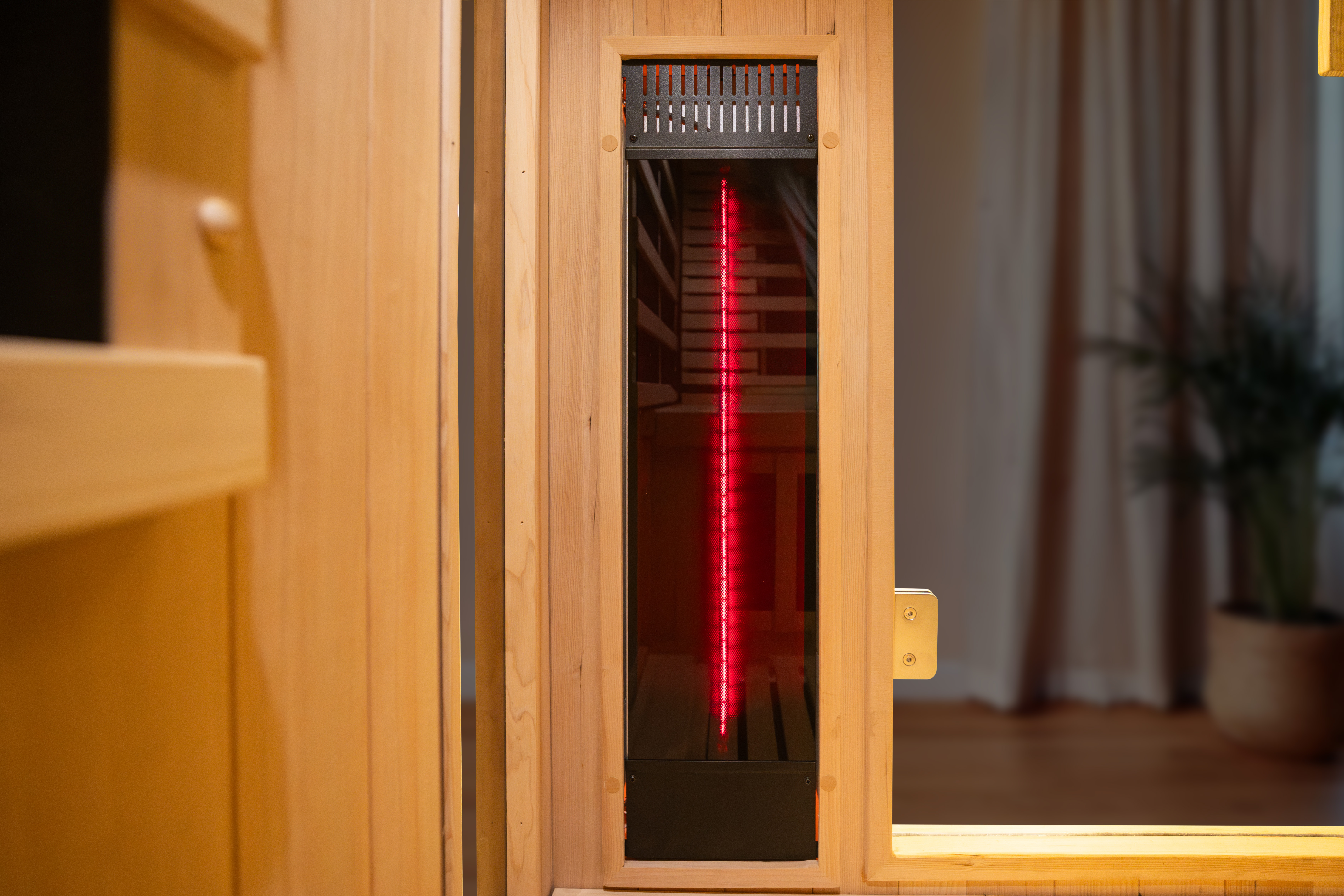 Close-up of a wooden infrared sauna door, partially open, showing a vertical red heating light inside.