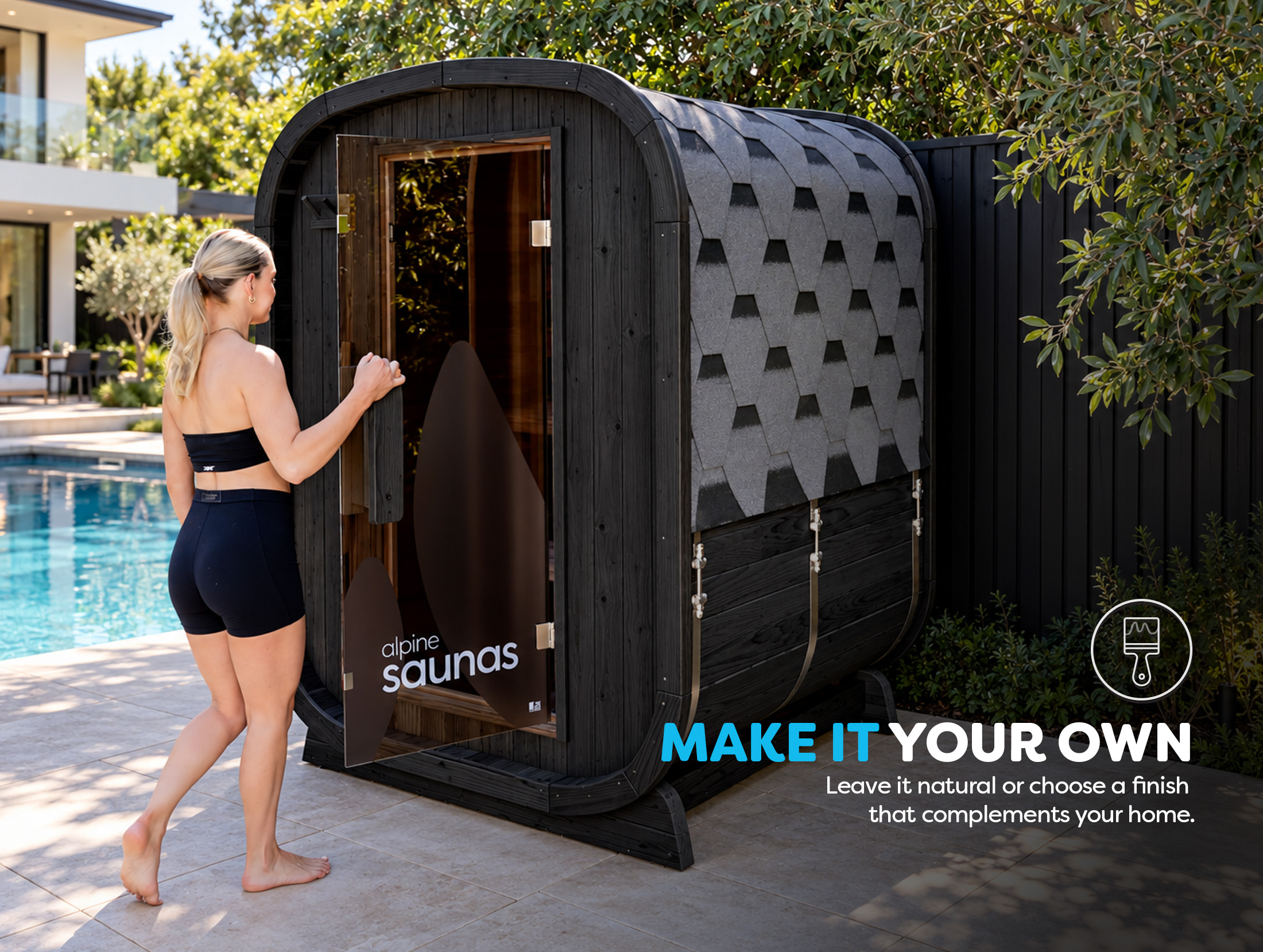 A woman in workout clothes opens the door of a modern outdoor wooden sauna next to a swimming pool, with trees and a house in the background.