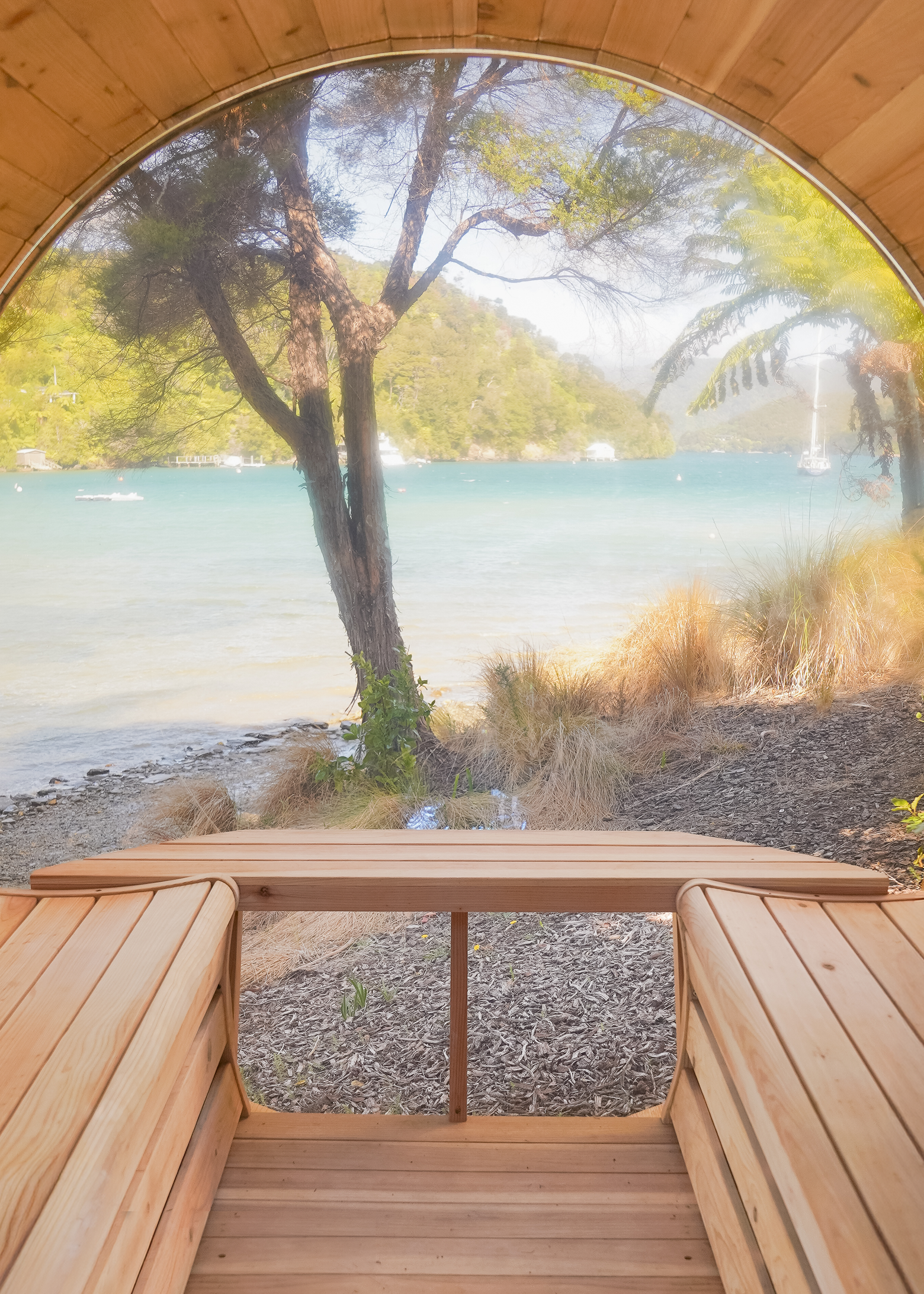 Curved wooden bench seating inside a structure with a large panoramic window overlooking a tranquil lakeside scene with trees and hills.