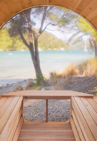 Curved wooden bench seating inside a structure with a large panoramic window overlooking a tranquil lakeside scene with trees and hills.