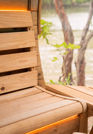 Close-up of a wooden bench with integrated orange lighting, set next to a window overlooking trees and greenery.