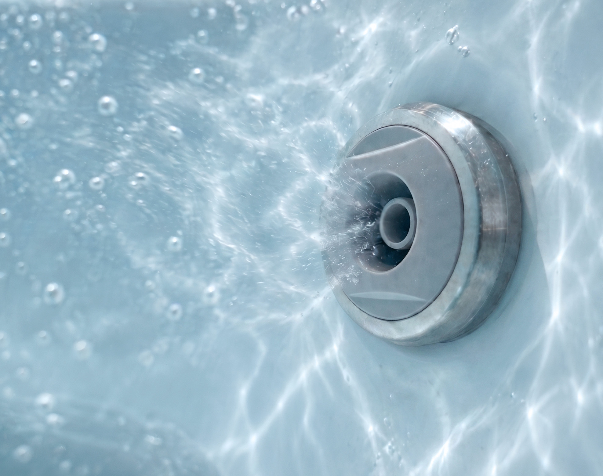 Close-up of a round metal water jet in a pool or hot tub, with bubbles and water flowing out.