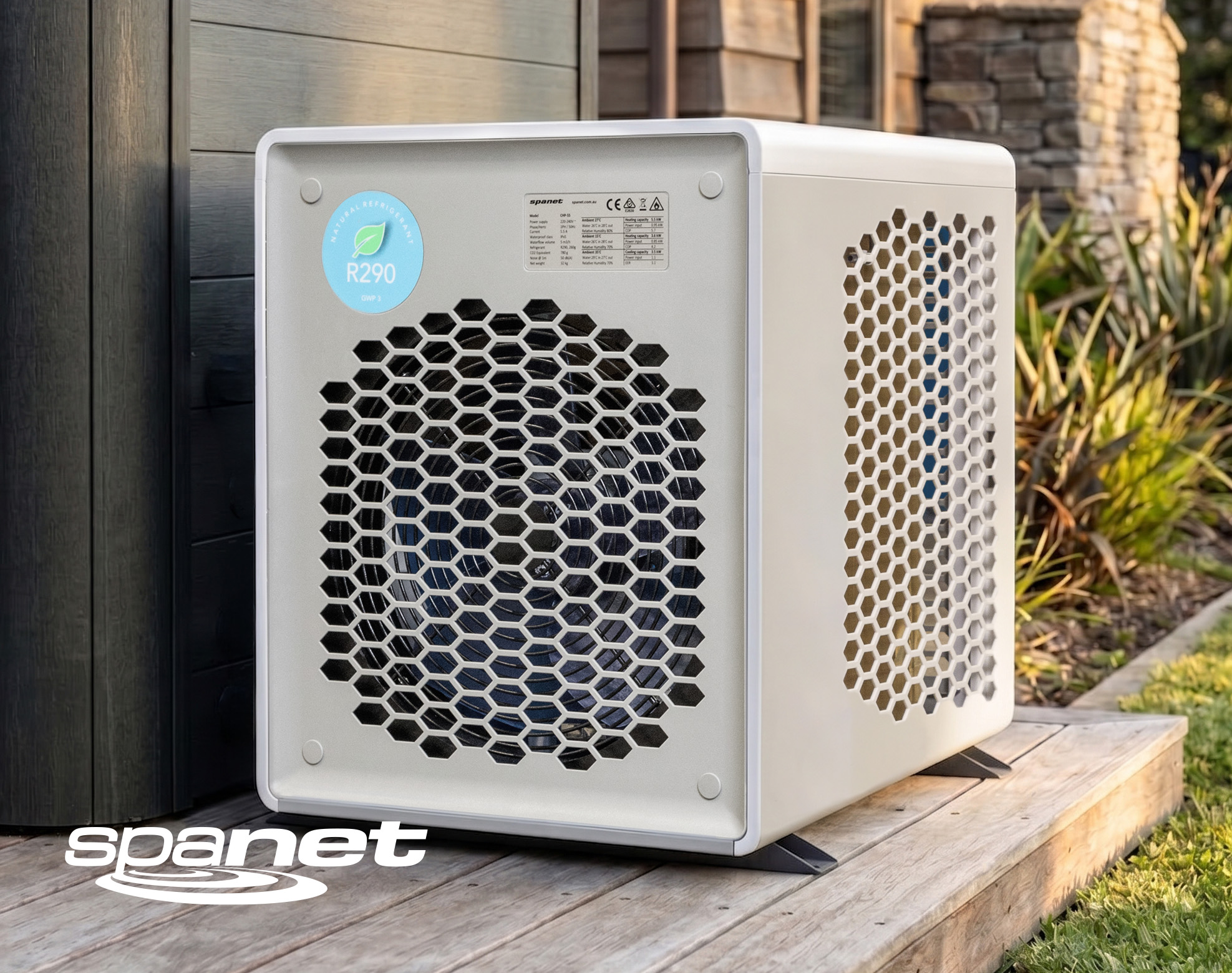 A white, box-shaped outdoor heat pump unit with honeycomb-patterned vents, labeled "R290" for natural refrigerant, sits on a wooden platform near a house. The "spanet" logo appears in the corner.