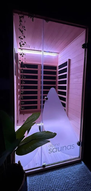 A modern wooden sauna with glass door, illuminated by soft purple lighting, and a plant in the foreground.