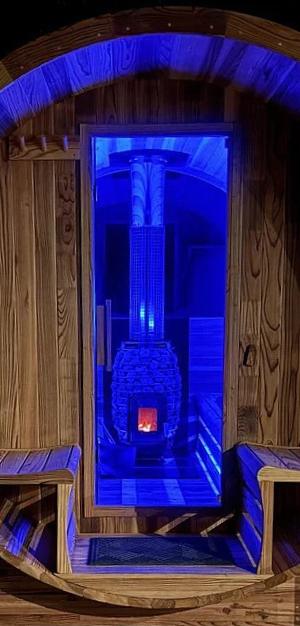 Wooden cabin-style structure with a glass door revealing a warmly lit interior and blue accent lighting, featuring a visible stove or heater inside.