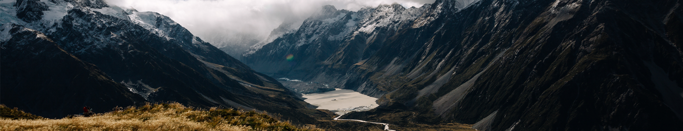 A dramatic mountain valley with snow-capped peaks, mist, and a winding river flowing through the landscape.